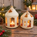 Two handmade cream ceramic house lanterns glowing with tealights in a festive setting
