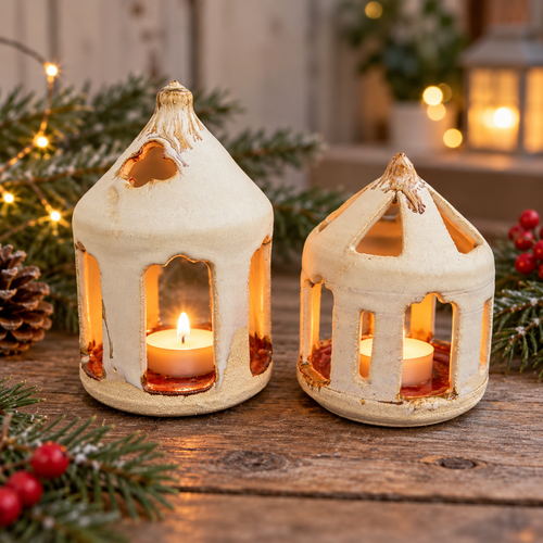 Two handmade cream ceramic house lanterns glowing with tealights in a festive setting